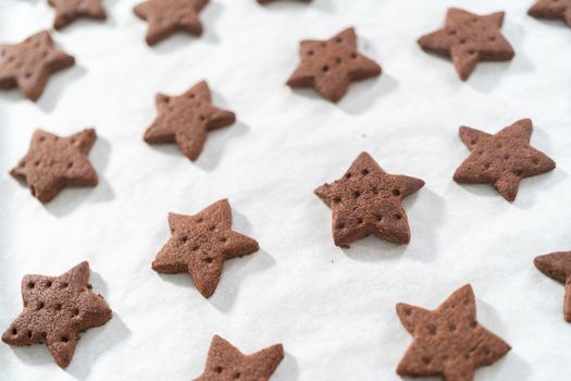 Cooling freshly star-shaped baked chocolate graham crackers on the baking sheet lined with parchment paper.