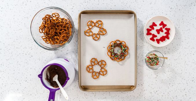 Flat lay. Dipping pretzels twists into melted chocolate to make a chocolate pretzel Christmas wreath.
