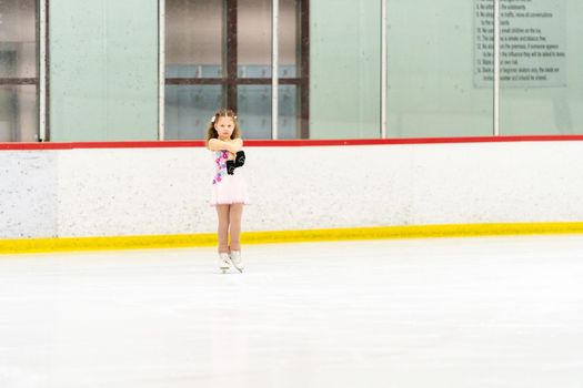 Little girl practicing figure skating on an indoor ice skating rink.