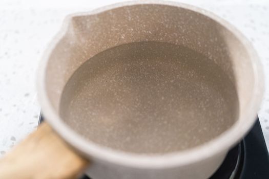 Melting chocolate chips and other ingredients in a glass mixing bowl over boiling water to prepare plain fudge.