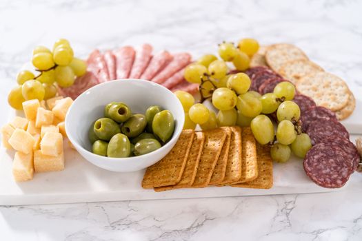 Cheese, meat, and crackers appetizer board on a marble surface.
