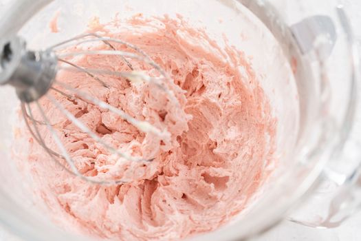 Whipping strawberry buttercream frosting in a stand-alone electric mixer with a whisk attachment.