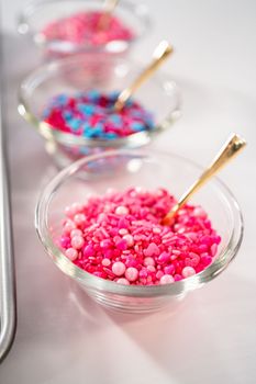 Drizzling melted chocolate over chocolate-dipped pretzels rods and decorating with sprinkles to make chocolate-covered pretzel rods for Valentine's Day.