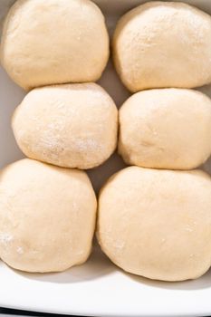 Rising dough in a white ceramic dish to prepare dinner rolls.