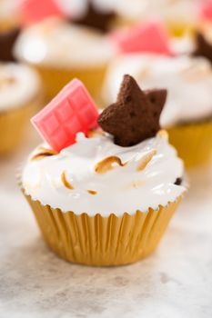 Gourmet s'mores cupcakes with meringue frosting and garnished with star-shaped chocolate graham cracker and a mini pink chocolate bar.