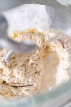 Kneading bread dough in a kitchen mixer with a dough hook to prepare dinner rolls.