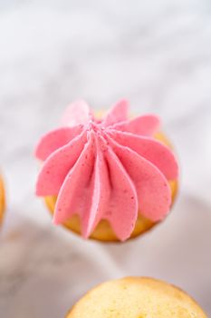 Piping ombre pink buttercream frosting on mini vanilla cupcakes.