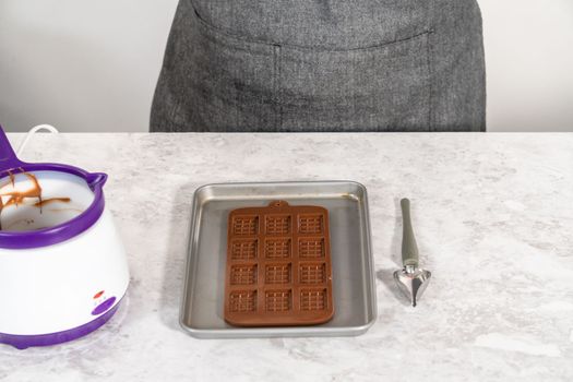 Filling chocolate silicone mold with melted dark chocolate to prepare gourmet mini chocolates with sprinkles.
