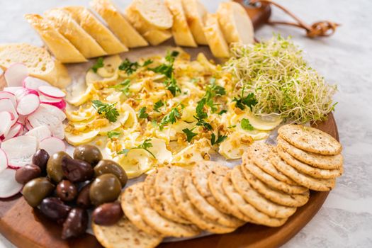 Butter board with vegetables and bread on a round wood cutting board.