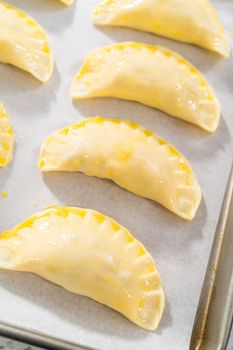 Brushing uncooked breakfast empanadas with eggs and sweet potato with egg wash.
