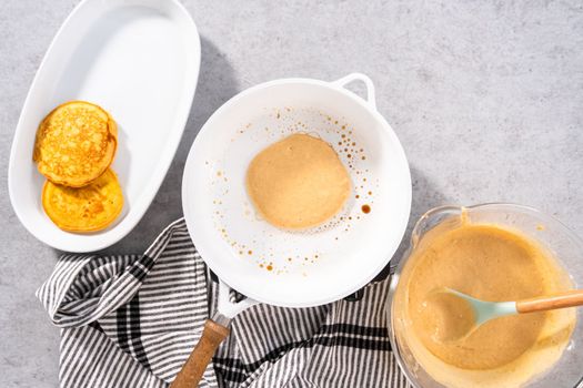 Flat lay. Frying pumpkin pancakes batter on a white frying pan.