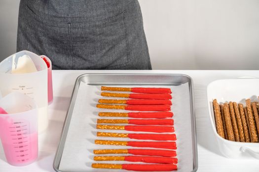Dipping pretzels rods into silicone cup with melted chocolate to make chocolate-covered pretzel rods for Valentine's Day.