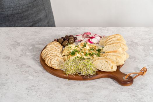 Assembling butter board with vegetables and bread on a round wood cutting board.