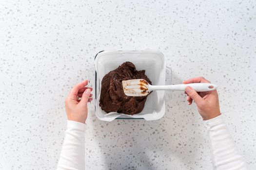 Flat lay. Pouring fudge mixture into the baking pan lined with parchment paper to prepare plain fudge.