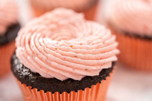 Chocolate cupcakes frosted with strawberry buttercream frosting.
