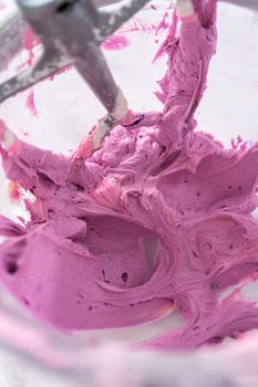 Mixing ingredients in kitchen electric mixer to make ombre pink buttercream frosting.