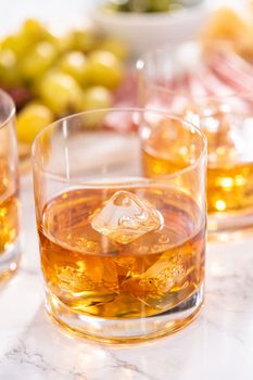 Scotch on the rocks in whiskey glass on a white marble surface.