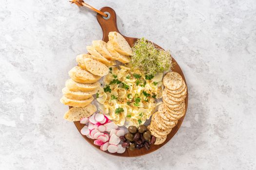 Flat lay. Butter board with vegetables and bread on a round wood cutting board.