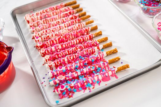 Drizzling melted chocolate over chocolate-dipped pretzels rods and decorating with sprinkles to make chocolate-covered pretzel rods for Valentine's Day.