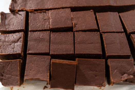 Cutting plain homemade fudge into small pieces on a white cutting board.