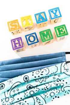 STAY HOME sign out of kids' alphabet blocks with homemade face masks on a white background.