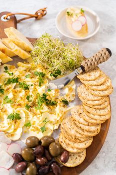 Butter board with vegetables and bread on a round wood cutting board.