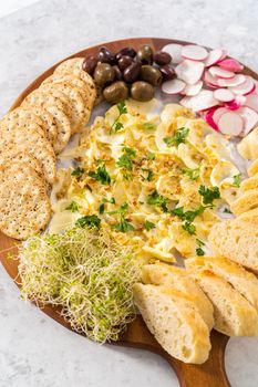 Butter board with vegetables and bread on a round wood cutting board.