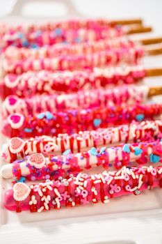 Chocolate-covered pretzel rods decorated with heart-shaped sprinkles for Valentine's Day.