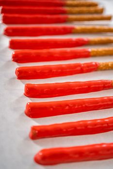 Dipping pretzels rods into silicone cup with melted chocolate to make chocolate-covered pretzel rods for Valentine's Day.