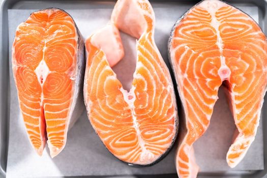Farm-raised salmon steaks on a cooking tray with a parchment paper.