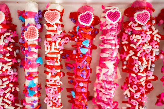 Chocolate-covered pretzel rods decorated with heart-shaped sprinkles for Valentine's Day.