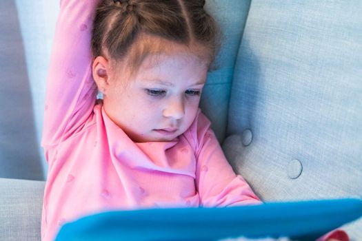 Little girl reading books on her tablet at homeschool.