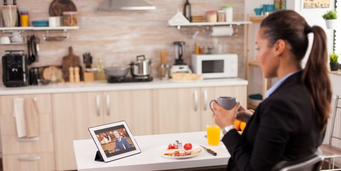 Business woman in a video call with her father during her father while eating breakfast. Using modern online internet web technology to chat via webcam videoconference app with relatives, family, friends and coworkers
