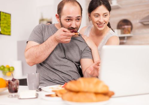 Young family receiving good news on email in the morning eating breakfast. Successful overjoyed euphoric entrepreneur at home in the morning, winner and business triumph