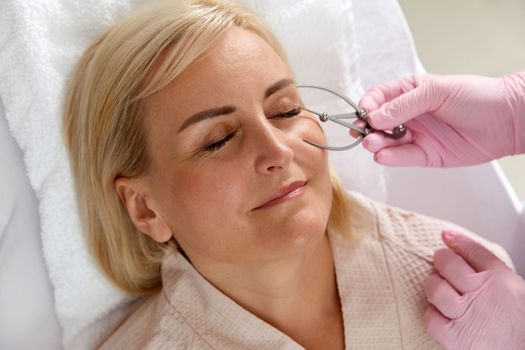 Woman getting her eyebrows angled by a beautician in beauty salon with instrument