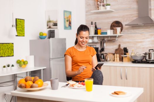 Woman taking the breakfast alone in modern kitchen. Woman drinking healthy and natural orange juice. Housewife drinking healthy, natural, homemade orange juice. Refreshing sunday morning