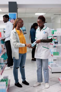 African american pharmacist helping woman choosing medications in drugstore. Client and pharmacy consultant chatting, customer buying medicaments, wide shot, all black team