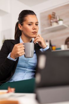 Freelancer drinking coffee in the morning on table top during breakfast using tablet computer. Business woman reading the last news online before going to work, using modern technology in the kitchen while eating a healthy meal