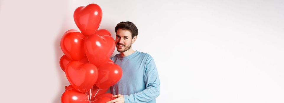 Romantic boyfriend bring red hearts balloons on Valentines day, surprise lover on date, standing over white background.
