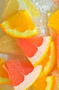 Fresh slices of grapefruit, orange fruit and honey pomelo on white background. Pieces of grapefruit, orange fruit and honey pomelo in sparkling water on white background, close-up. Vertical macro image. Top view, flat design. Summer fruit background.