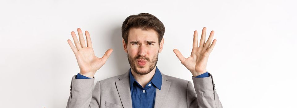 Close-up of disappointed and disgusted businessman raising hands up, grimacing from dislike and aversion, standing reluctant on white background.