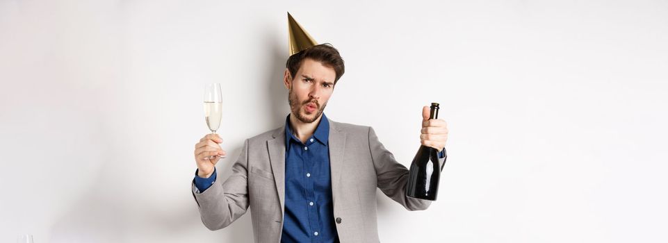 Celebration and holidays concept. Happy man in suit having fun at party, wearing birthday hat, dancing with champagne and drinking alcohol.