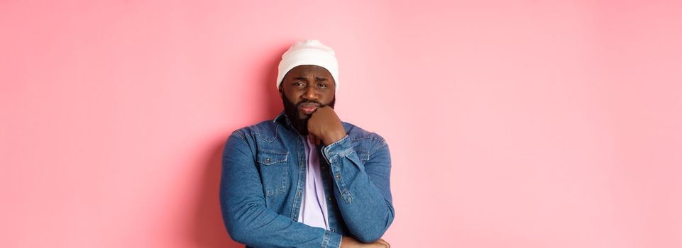 Young african-american man look with pity and concern at camera, frowning and feeling uneasy, standing over pink background.