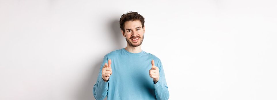 Well done. Smiling handsome man pointing fingers at camera to congratulate or praise good work, looking proud, standing over white background.