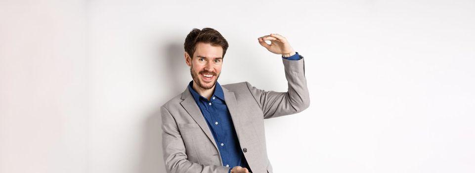 Successful businessman showing big size, shape large object and smiling pleased, standing on white background in suit.