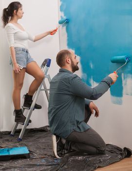 Wife using the ladder helps her husband to paint apartment wall using roller brush. Apartment redecoration and home construction while renovating and improving. Repair and decorating