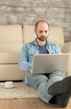 Man working on laptop sitting on living room rug.
