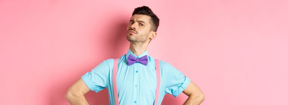 Proud and confident caucasian guy with moustache and bow-tie, looking arrogant with chin up, frowning and looking at camera, standing on pink background.