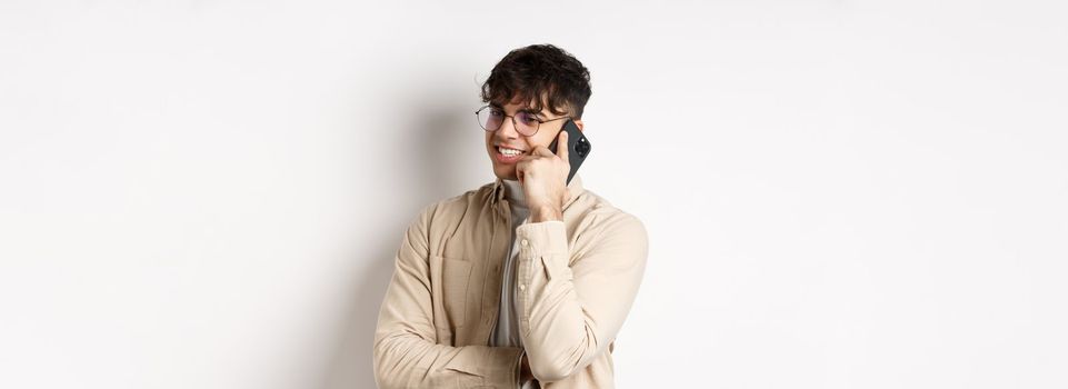 Real people concept. Handsome modern man talking on mobile phone, look aside and holding smartphone near ear, standing on white background.