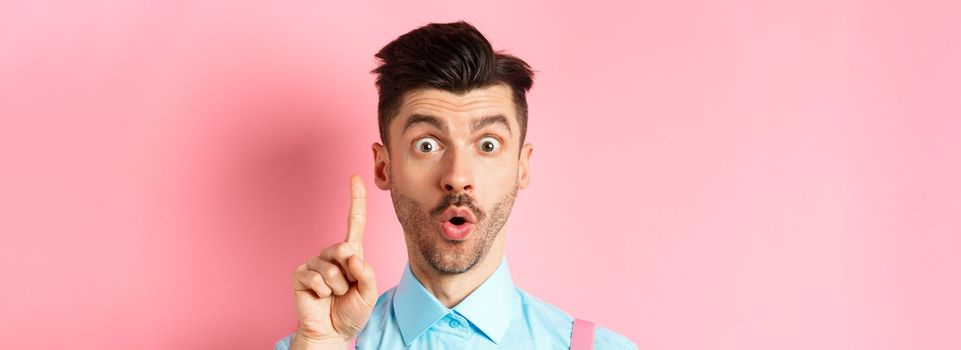 Close-up of excited guy pitching an idea, raising finger and saying suggestion, have a plan, standing on pink background. Copy space